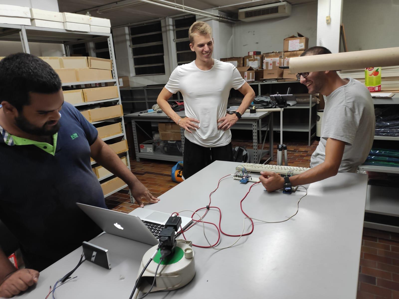 Three of us testing the Omnia proof of concept in the workshop, laughing around a table covered with a laptop, breadboards, and a keyboard wired together as a makeshift network computer.
