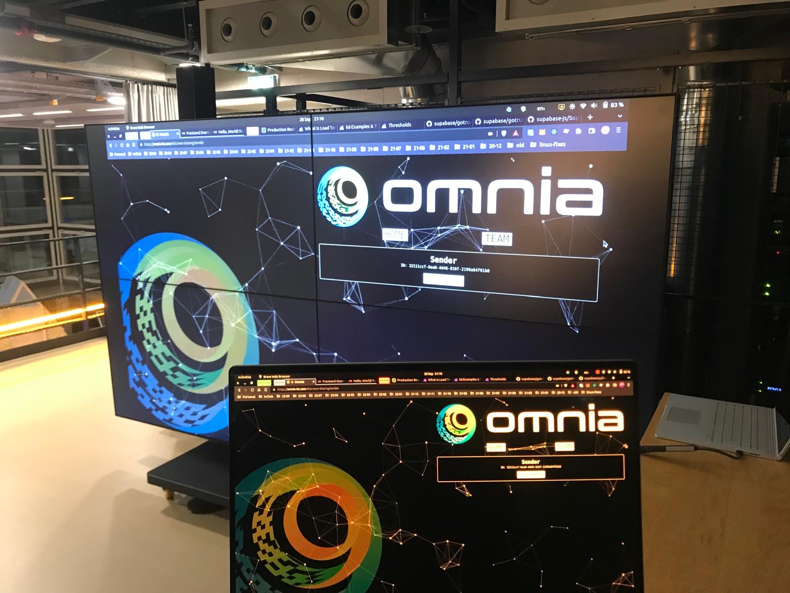 Omnia Share connecting a laptop to the big screen at SPH: the laptop in the foreground runs the Omnia "Sender" page in the browser, screen-sharing peer to peer to the wall-sized display behind it.
