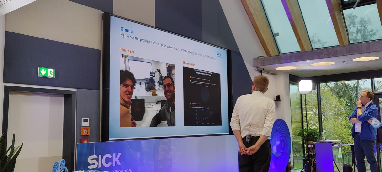 Presenting Omnia at SICK: a slide reading "Omnia — Figure out the problems of your production line, simply by asking questions to the machines," with the team and the solution.