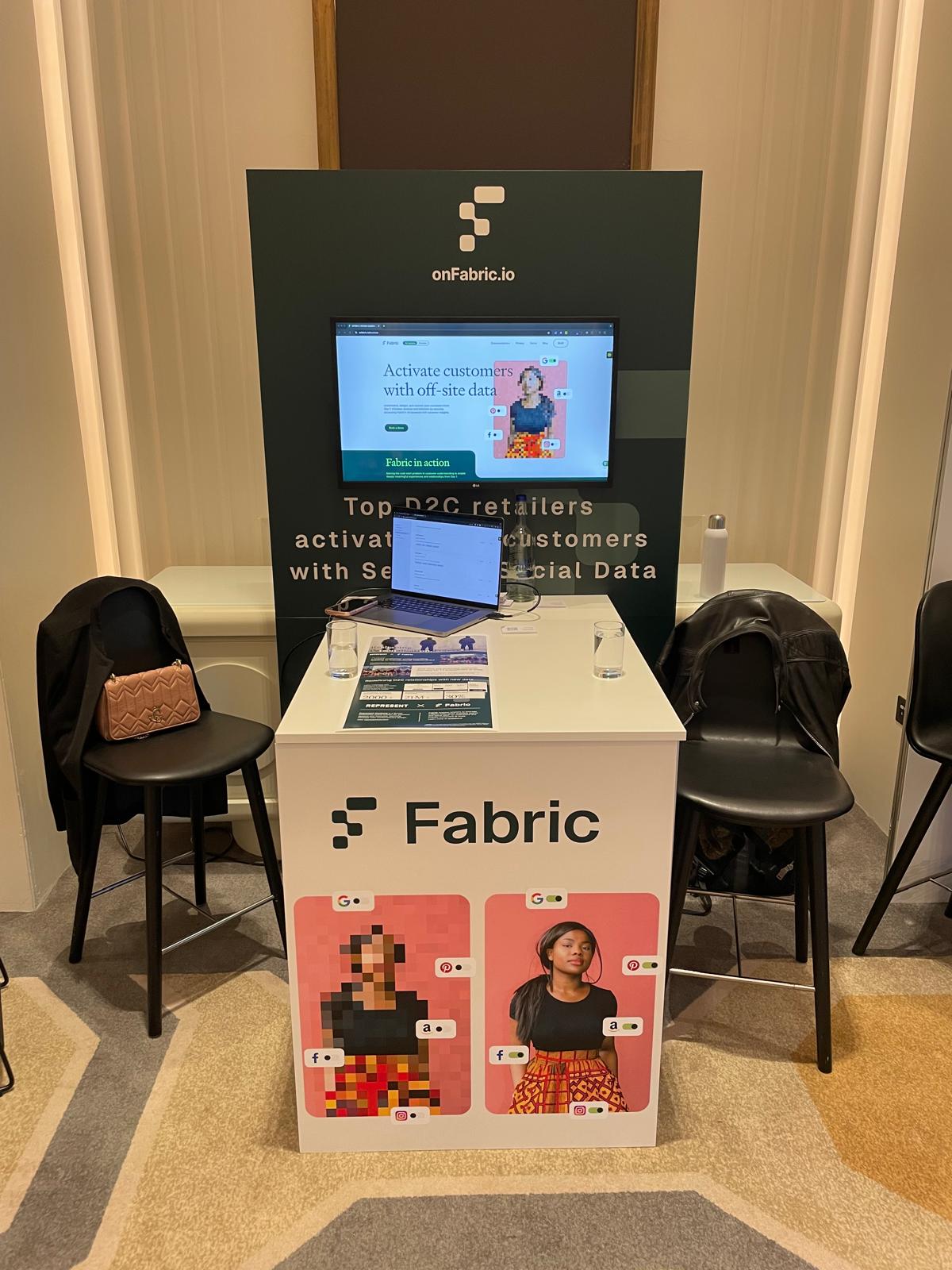 The booth, with the demo running on screen and the Represent × Fabric case study on the counter.